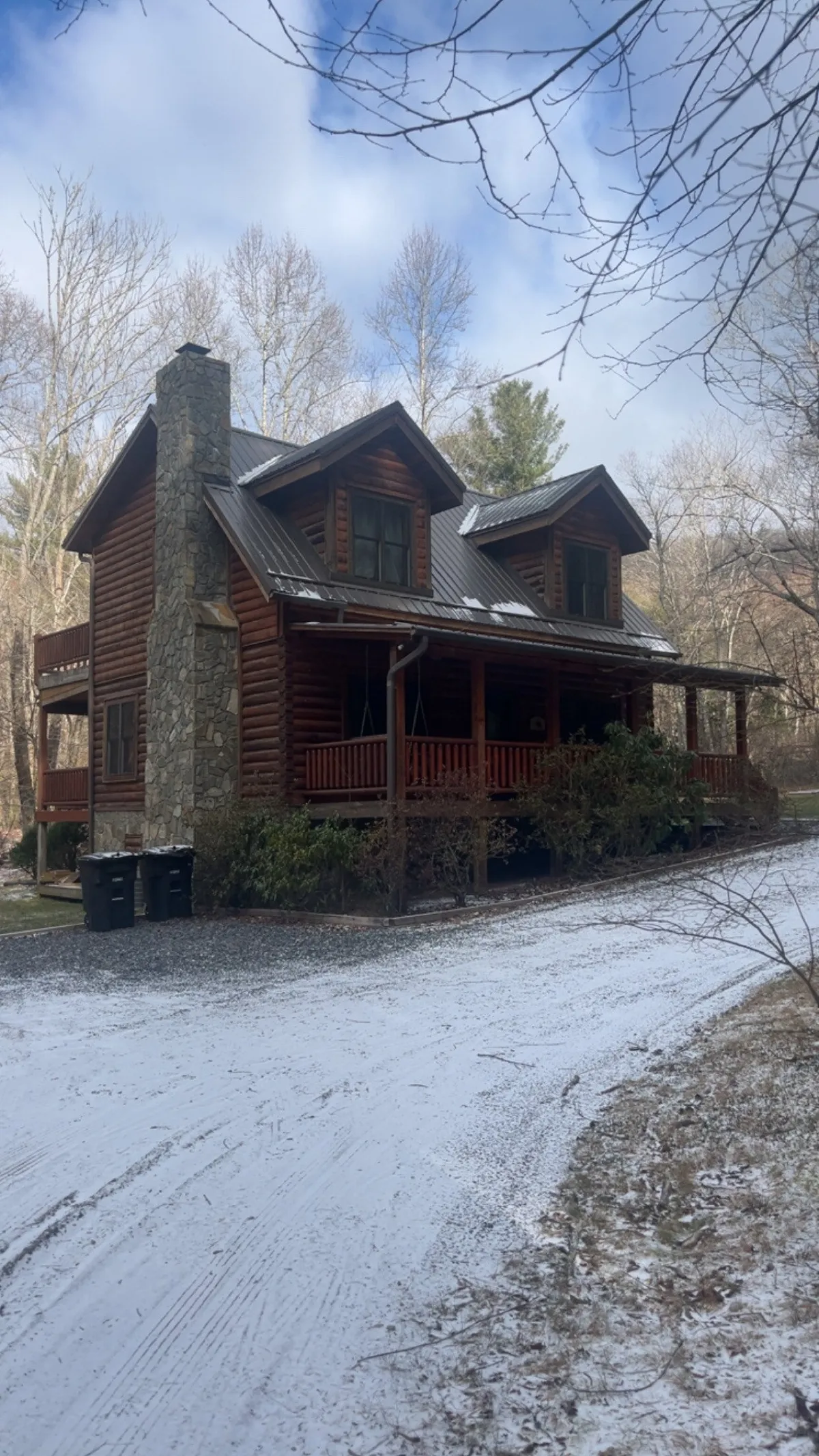 This image showcases the exterior of the log cabin, featuring a welcoming front porch swing and a sturdy stone chimney. The surrounding landscape hints at nearby trails and natural beauty, perfect for pet-friendly exploration.