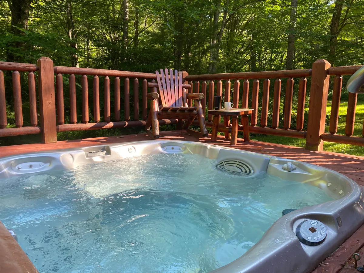 This image showcases an inviting outdoor hot tub surrounded by a wooden chair and small table. The tranquil scene is enhanced by soft natural light, and the hot tub is positioned to take advantage of both morning coffee moments and stargazing at night.