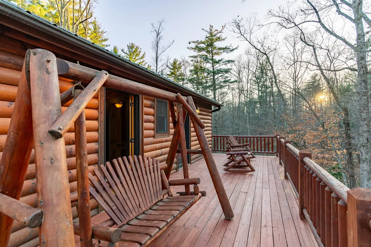 This exterior shot captures a wooden deck with swings, surrounded by mature trees and bathed in the soft glow of sunset. The scene evokes moments of relaxation as family members might sip coffee or read a book in the swing, enjoying nature and the peaceful mountain environment.