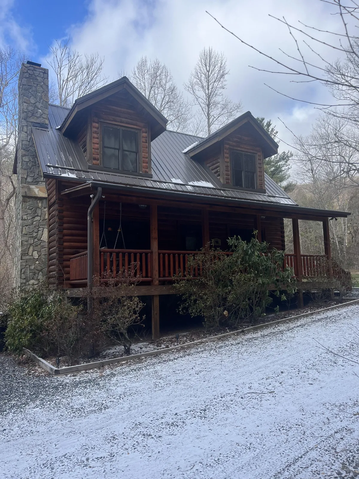 A charming log cabin structure with a stone chimney and a front porch, surrounded by trees. The scene evokes warmth and community, with the porch serving as an ideal spot for gathering by the fire pit or enjoying quiet conversations after a day of adventure.
