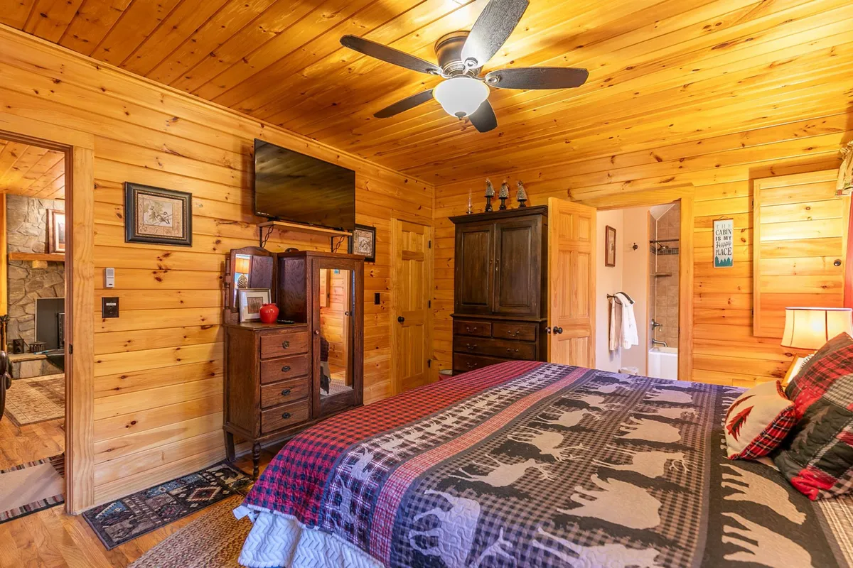 A cozy bedroom with wood paneling, a bed dressed in fresh, patterned linens, a wall-mounted TV, and a mirror. The atmosphere exudes comfort and relaxation, ideal for unwinding after a day outdoors.