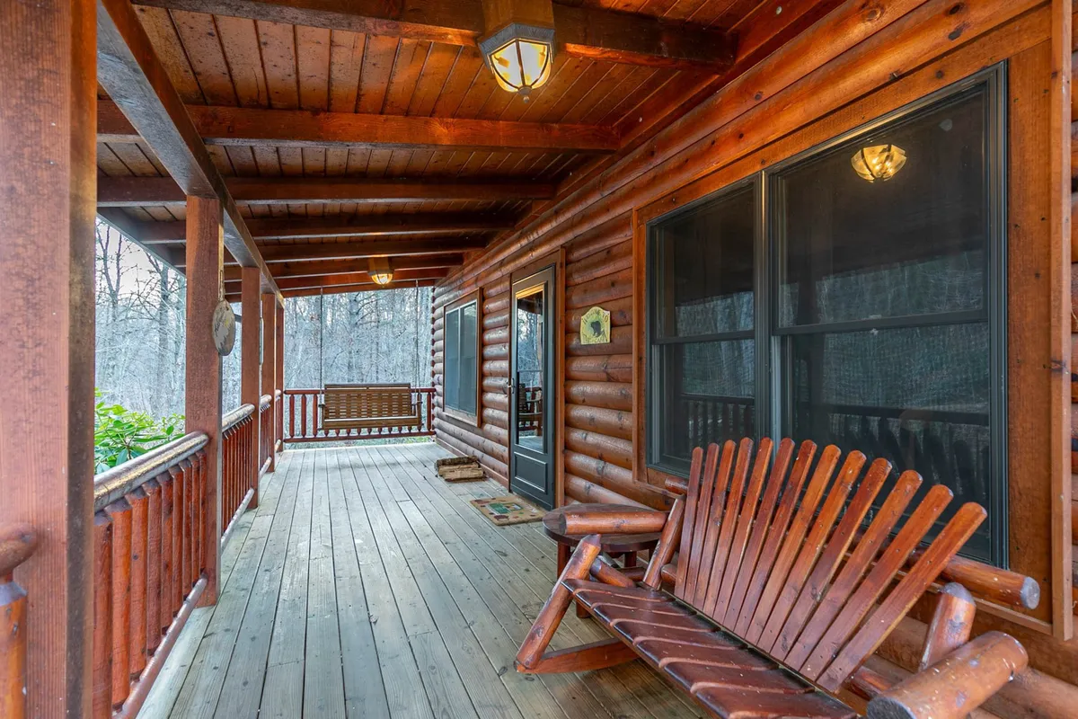 A cozy porch scene with a wooden rocking chair, swing bench, and log cabin details. The setup invites relaxation and socialization, hinting at leisurely moments spent outside.