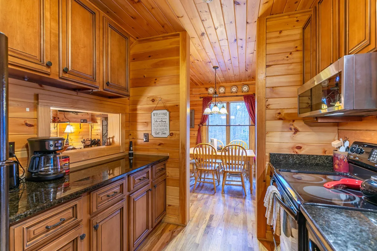 An interior shot of the kitchen and dining area, featuring granite countertops, wooden cabinets, a dining table, and a window with curtains. The space feels warm and well-prepared for guest arrivals, suggesting readiness with supplies, linens, and towels.