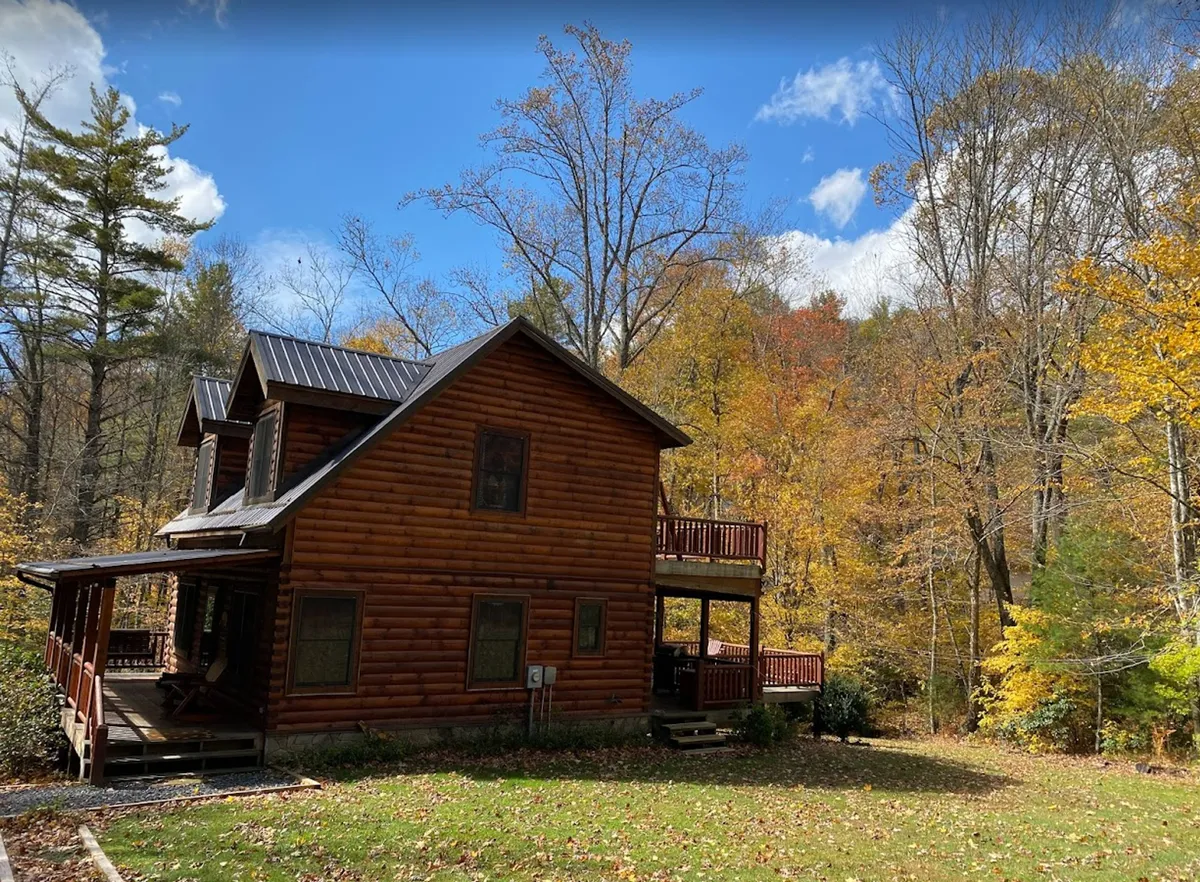 A log cabin nestled among vibrant autumn foliage, with a deck area overlooking nature. The setting is serene, perfect for relaxing after a day of hiking, biking, or kayaking, and visually connects the property to the outdoors.