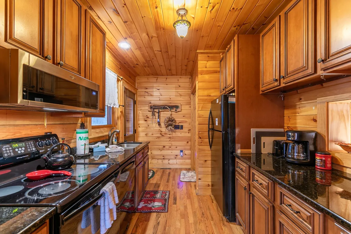 A cozy kitchen scene with stainless steel appliances, dark granite countertops, wooden cabinetry, and gleaming wooden floors. The space is both modern and welcoming, ideal for preparing meals and gathering with loved ones.